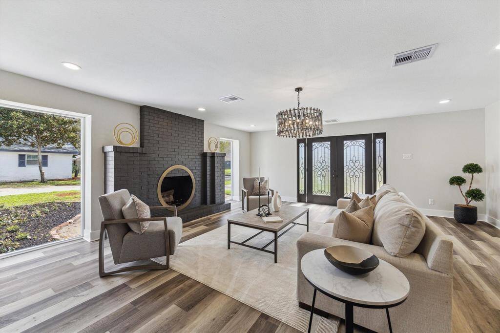 This elegant living room provides the perfect setting to entertain in style, featuring luxury vinyl plank flooring, neutral paint, chic lighting, floor-to-ceiling windows, a romantic wood-burning fireplace and a striking chandelier. The spacious layout offers endless possibilities to customize and make it your own.