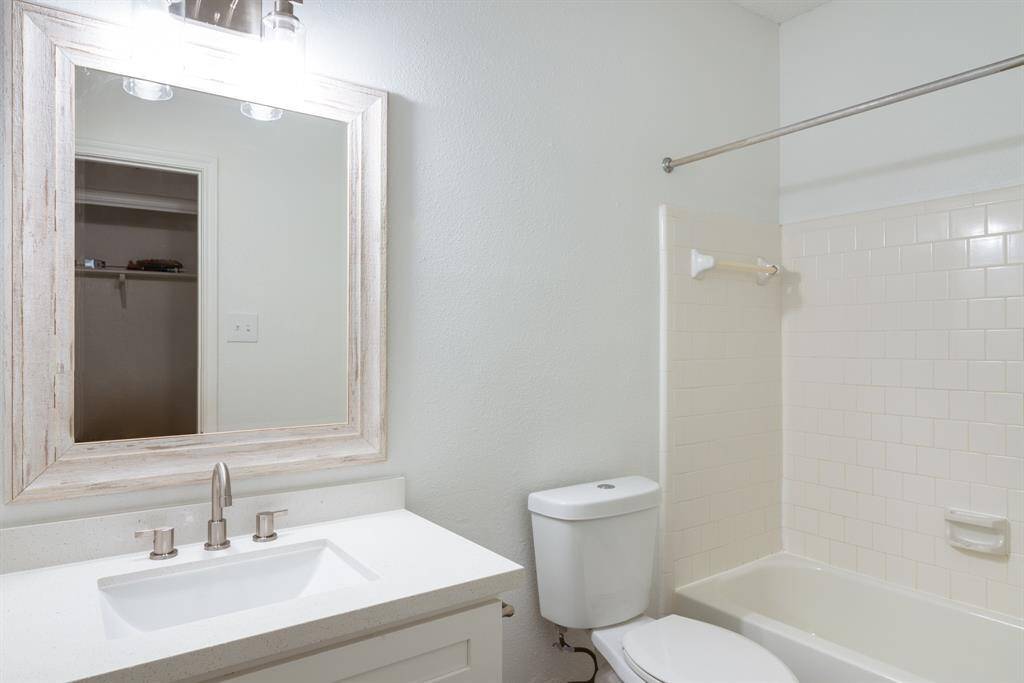 This bathroom features a modern design with a white vanity and countertop, a large framed mirror, and a bathtub-shower combo with tiled walls. It offers a clean and bright appearance, ideal for a refreshing space.