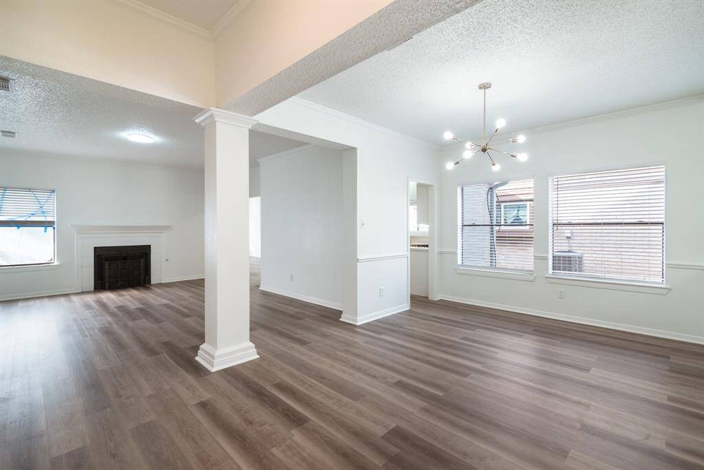 This spacious home features an open living and dining area with elegant wood flooring, abundant natural light, and a modern chandelier. The room includes a cozy fireplace, large windows, and a neutral color scheme for versatile styling.