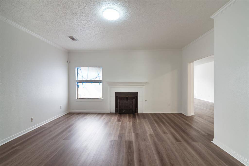 This spacious living room features modern wood flooring, a cozy fireplace, and ample natural light from a large window. The neutral walls offer a blank canvas for personalization.