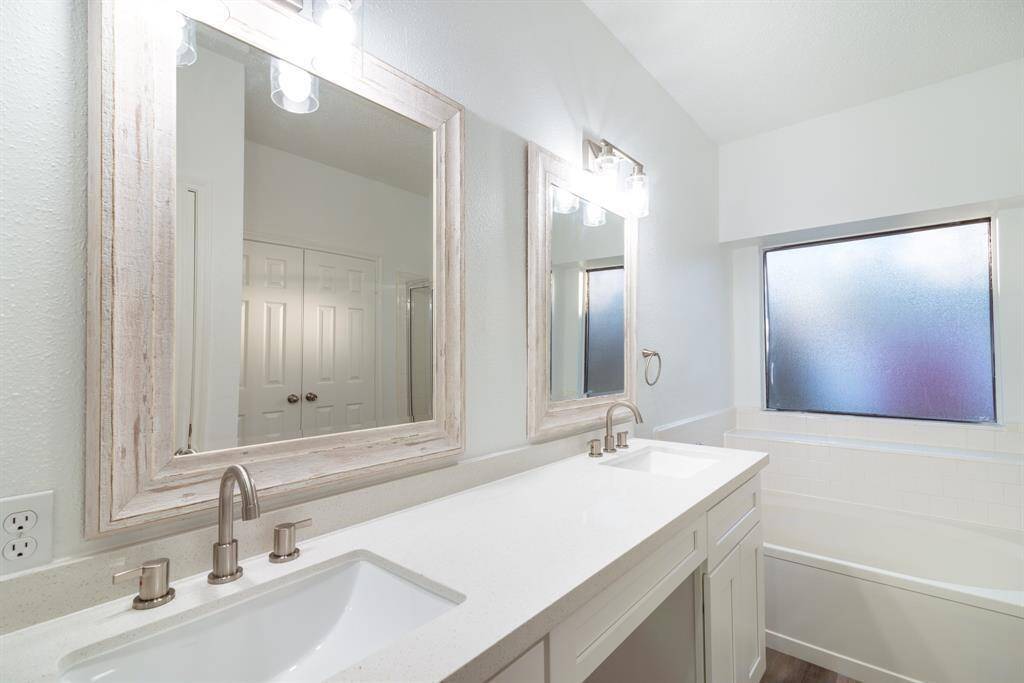 This bathroom features a modern, bright design with dual sinks, sleek countertops, and framed mirrors. It has a frosted window for privacy and plenty of natural light, complementing the clean, white cabinetry.