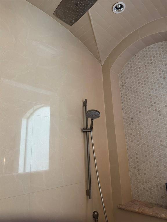Shower in Primary bath has beautiful groin ceiling and a rain shower head and hand held showerhead. A bench and a shelf for shampoo are on the right.