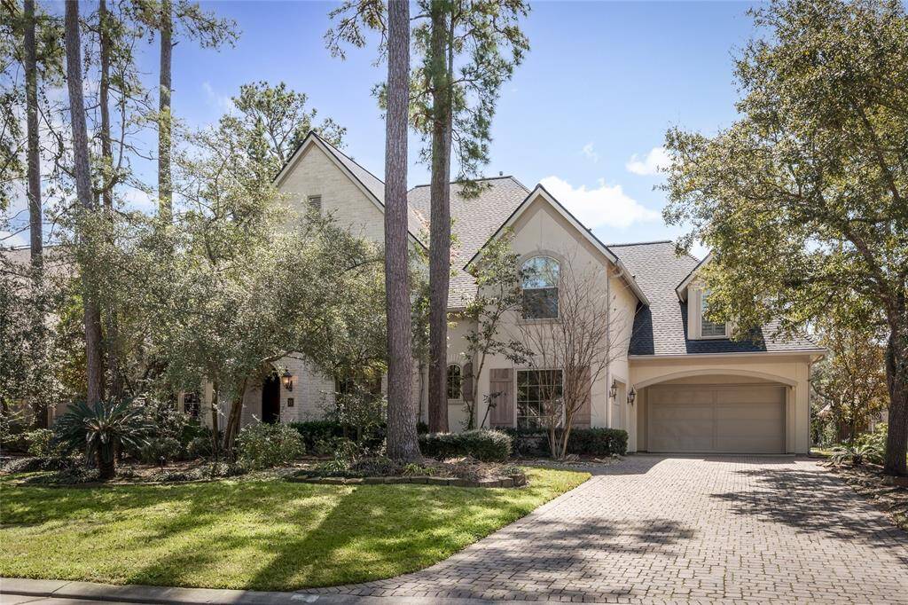 This photo shows a charming two-story home with a light brick exterior, nestled among mature trees. It features a well-maintained front yard, a spacious driveway, and an attached three-car garage. The house has a classic, inviting appearance with large windows and a gabled roof.