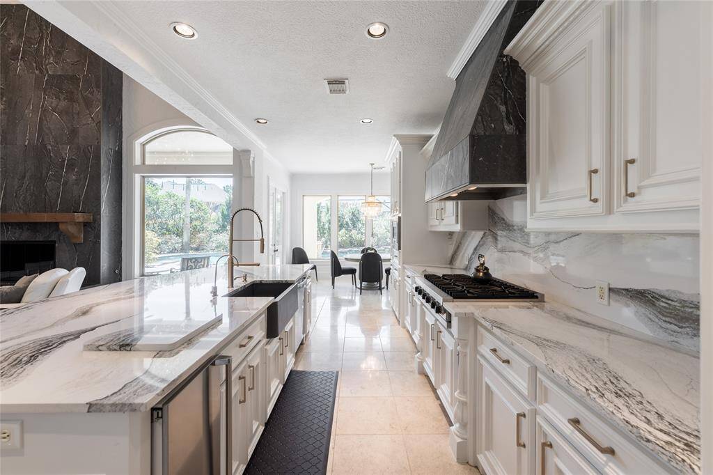 This modern kitchen features sleek quartz countertops, ample white cabinetry, and a large gas stove. It opens to a bright dining area with large windows, offering plenty of natural light and a view of the outdoors.