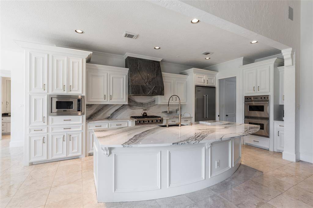 This photo showcases a spacious, modern kitchen with white cabinetry, a large quartz island, stainless steel appliances, and elegant lighting. The open layout and sleek design make it ideal for cooking and entertaining.