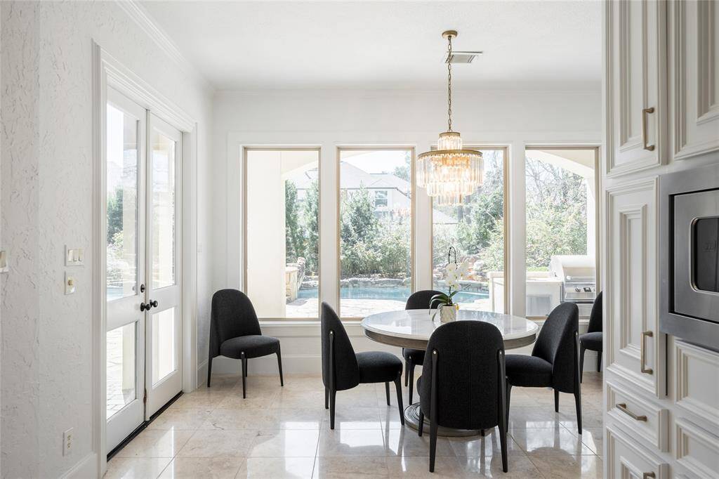 Bright breakfast area featuring large windows offering a view of the backyard pool. Elegant chandelier above and tile flooring enhance the airy atmosphere.