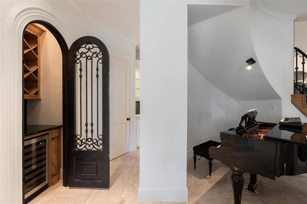 This elegant home features a cozy wine nook with a stylish iron door and built-in wine fridge. Adjacent is a sophisticated area under the stairs, perfect for a piano, with soft lighting and a modern design.