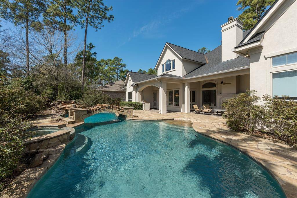 This beautiful home features a spacious backyard with a stunning pool and hot tub, surrounded by a natural stone patio. The exterior boasts a modern, elegant design with a covered patio area perfect for outdoor entertainment. Lush greenery and tall trees provide privacy and a serene atmosphere.
