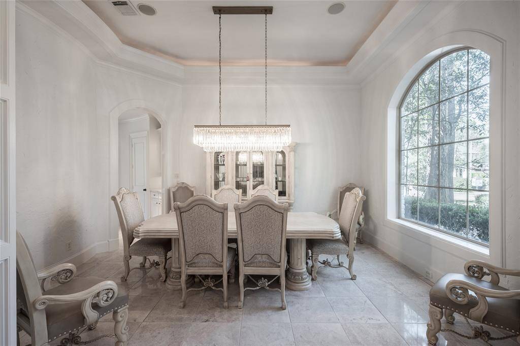 This elegant dining room features a large window with garden views, and a classic chandelier creating a bright and sophisticated atmosphere.