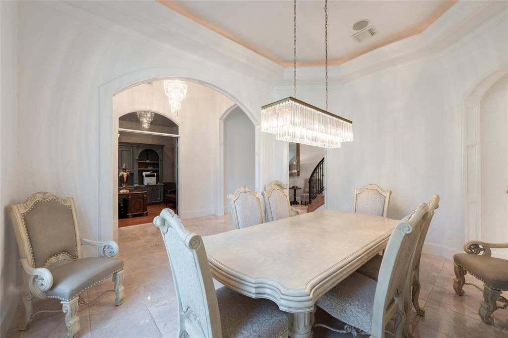 This elegant dining room features a luxurious chandelier, ornate chairs, and a classic table. The arched doorway leads to adjacent spaces, enhancing flow and sophistication.