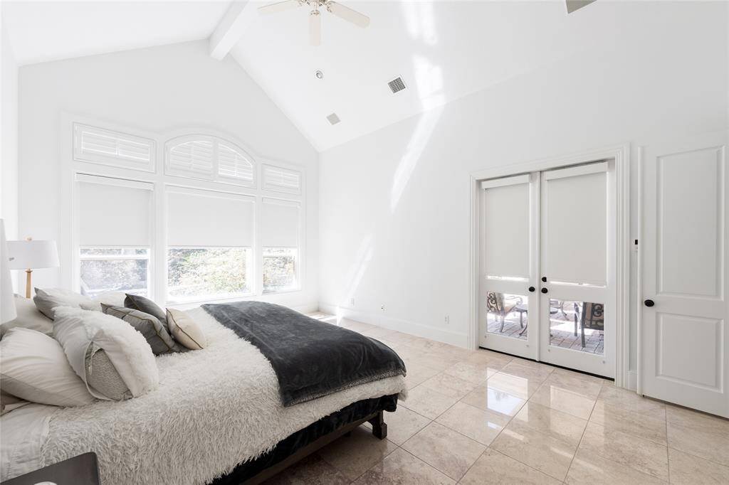 Bright and spacious primary bedroom with high ceilings, large windows, and polished tile floors. It features a cozy bed and double doors leading to a patio, offering ample natural light and a serene atmosphere.