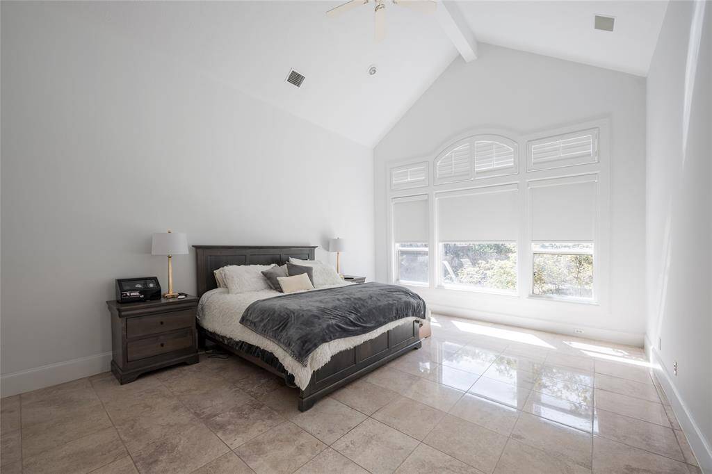 Spacious Primary bedroom with high ceilings and large arched windows, allowing plenty of natural light. Features a sleek, modern design with travertine stone flooring and neutral tones, creating a bright and inviting atmosphere.