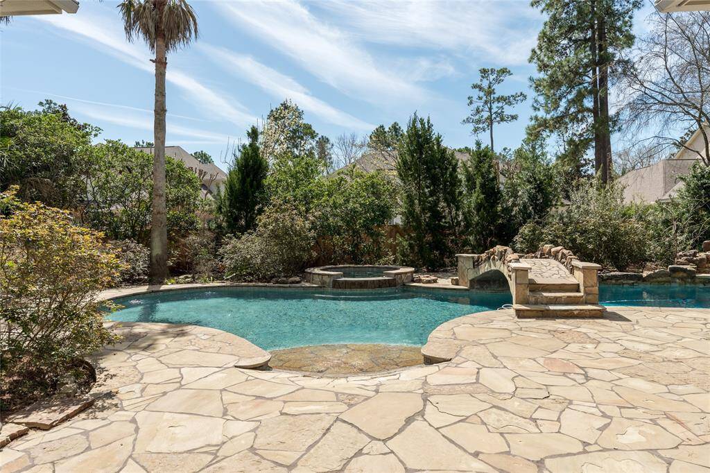 This backyard features a spacious swimming pool with a stone patio and a charming bridge. Lush greenery and trees provide privacy and a serene atmosphere.