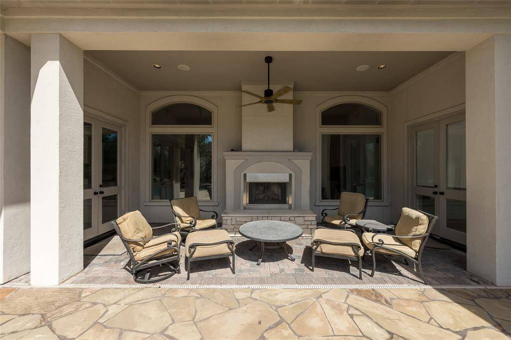 This outdoor space features a covered patio with a ceiling fan, and a cozy fireplace. It's perfect for relaxing or entertaining in a covered area.