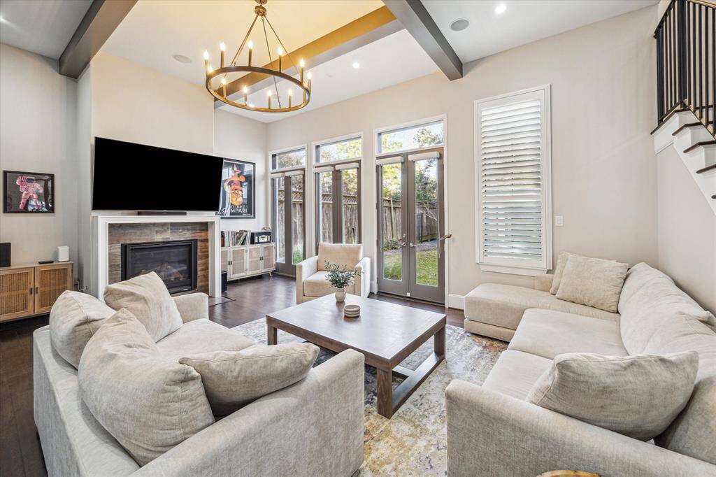 Spacious living area with soaring ceilings, rich wood floors, and abundant natural light through floor-to-ceiling windows. A sleek gas fireplace serves as the focal point of the room.
