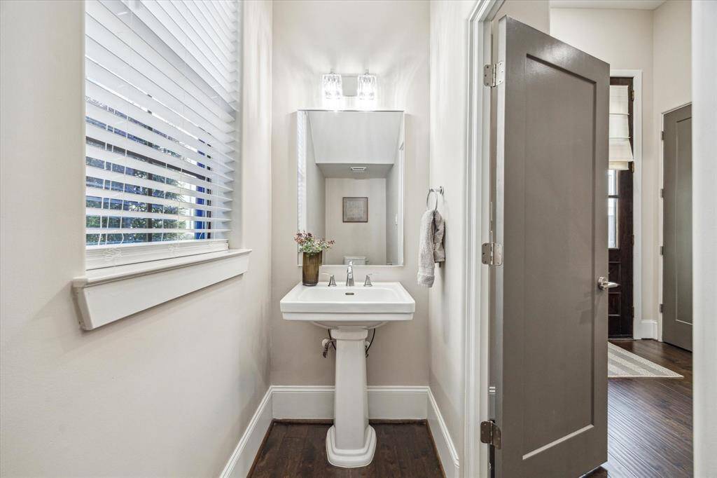 Chic powder bath with pedestal sink and designer lighting is conveniently located on the main level for guests. Natural light adds warmth and elegance.