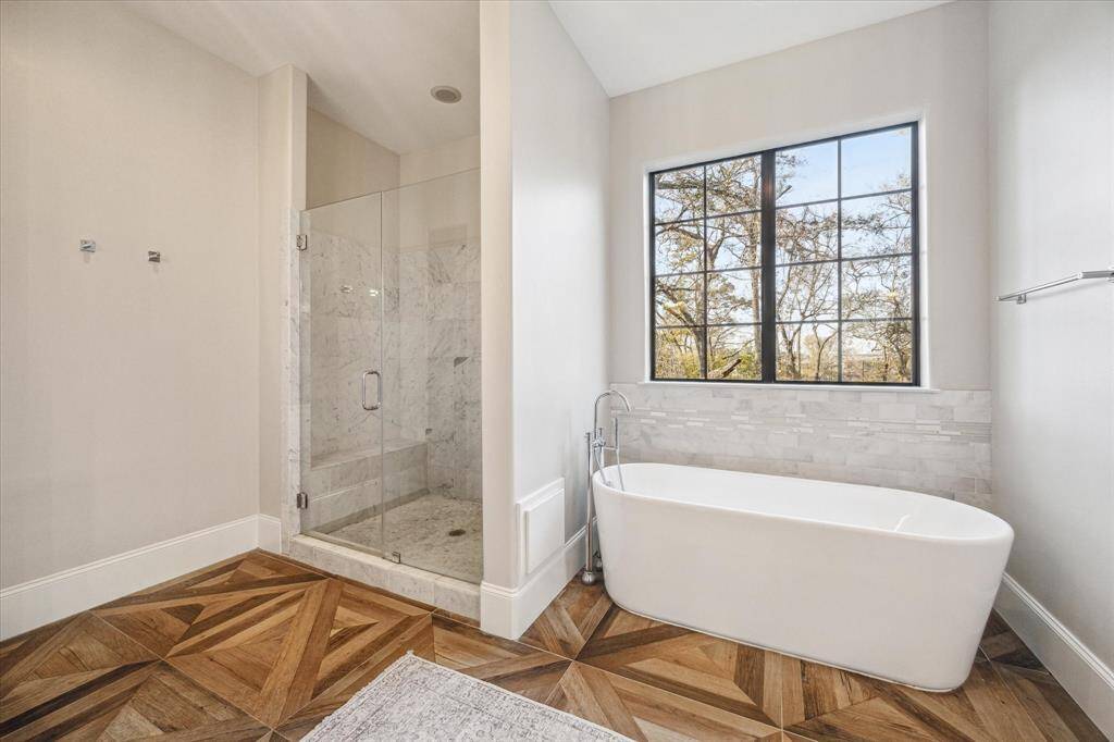 Spa-inspired bath with a frameless glass shower and freestanding soaking tub positioned beneath a large picture window. This space is thoughtfully designed for comfort and relaxation.