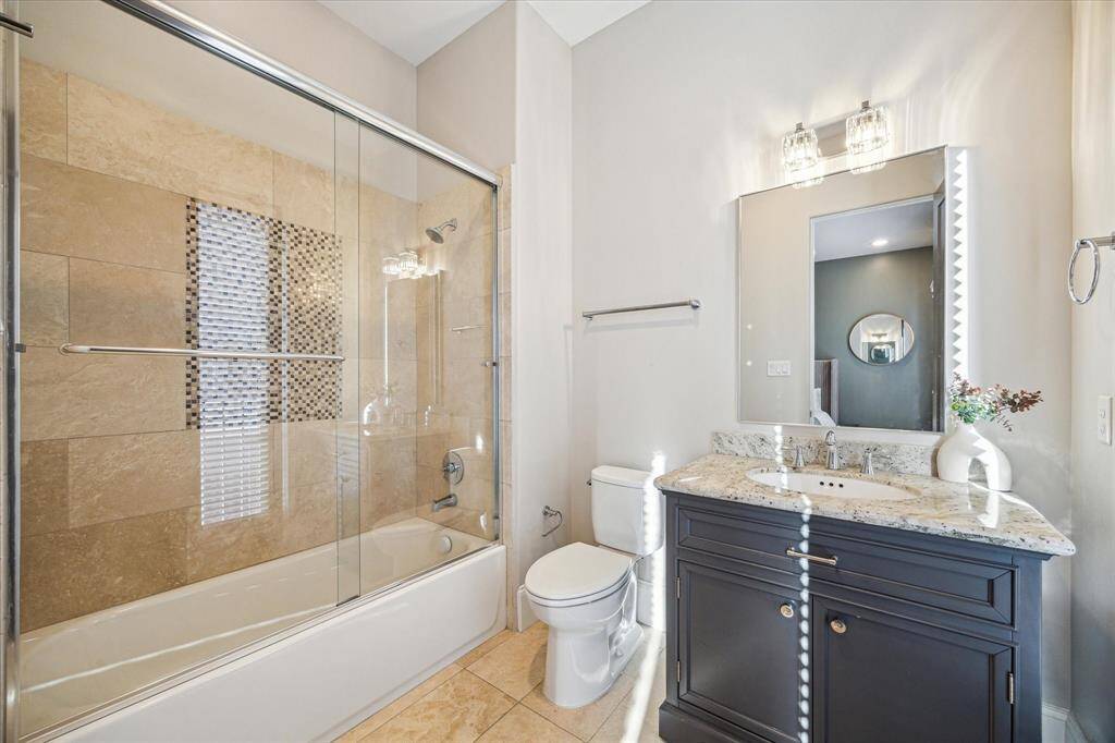 Well-appointed secondary bathroom features granite countertops, elegant lighting, and a combination tub/shower with decorative tile inlay. Clean and modern finishes throughout.