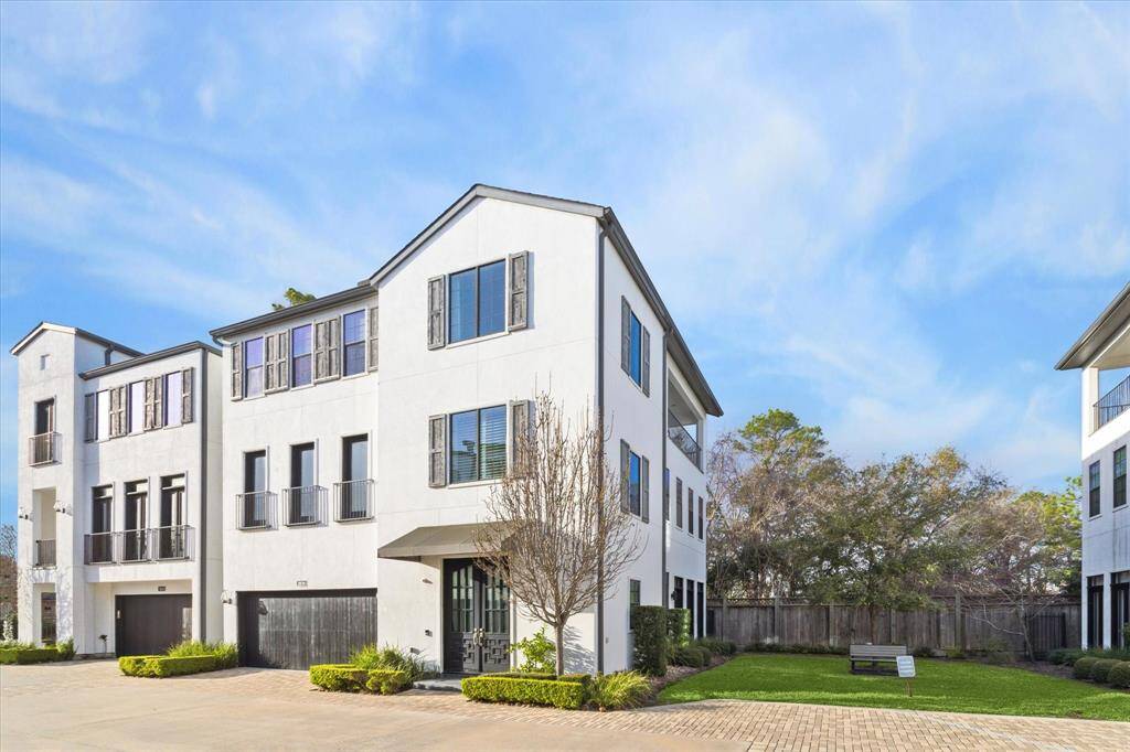Modern three-story residence with clean stucco exterior, contrasting shutters, and a striking black double front door. The home includes a spacious two-car garage and is part of a gated community.