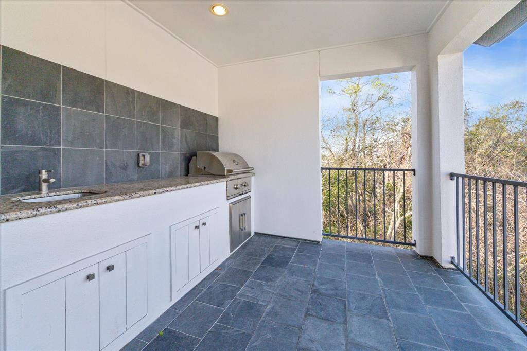 The outdoor kitchen includes a built-in grill, sink, and granite countertop — perfect for alfresco dining with treetop views.