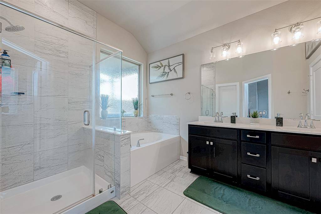 This modern bathroom features a spacious shower, a separate bathtub, dual sinks, and elegant tile flooring. Large windows provide natural light, enhancing the clean, contemporary design.