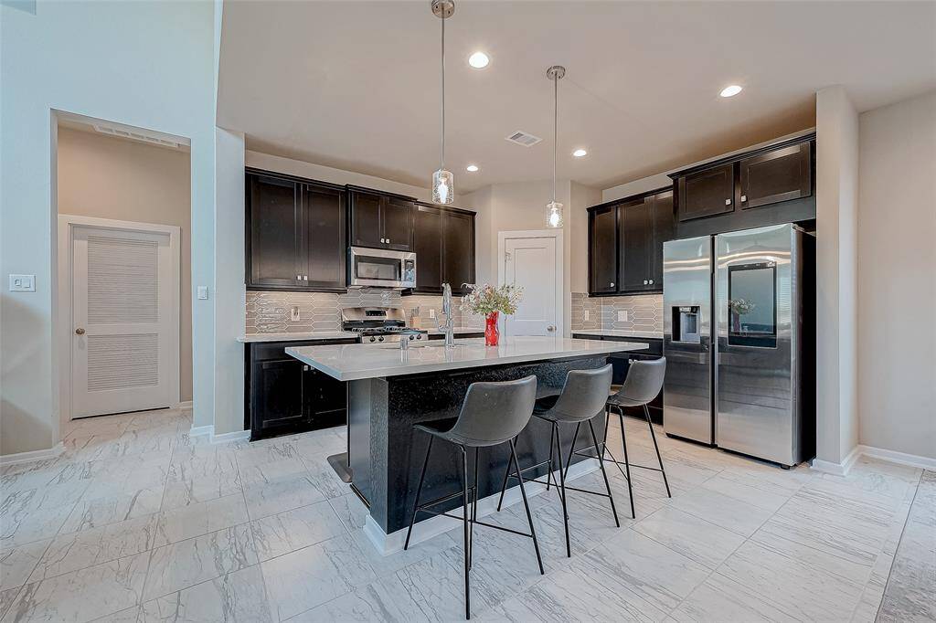 Modern kitchen with sleek cabinetry, stainless steel appliances, and a central island with seating. The space is well-lit with pendant lights and features light tile flooring, offering a clean and stylish look.