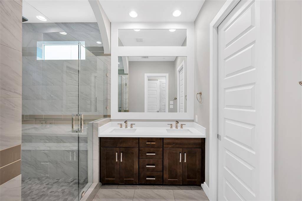 The bright, stylish primary bathroom with a double vanity, great lighting and a spacious walk-in shower with glass doors.