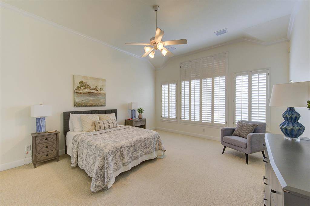 This spacious first-floor primary suite is a private retreat, featuring plush carpeting that adds warmth and comfort underfoot. Large picture windows with plantation shutters invite an abundance of natural light while providing privacy and a classic touch. The high ceilings enhance the room’s airy feel, creating a serene space to unwind. With plenty of room for a king-sized bed and additional seating, this suite is both functional and luxurious—perfect for relaxation at the end of the day.