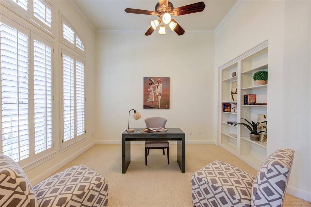 A sophisticated home office with French doors for privacy, plush carpeting, and large windows with Plantation shutters allow natural light to flood the space.