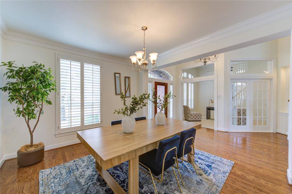 This elegant dining space boasts rich wood flooring, a stylish chandelier, and plantation shutters, creating the perfect setting for intimate dinners or large gatherings.