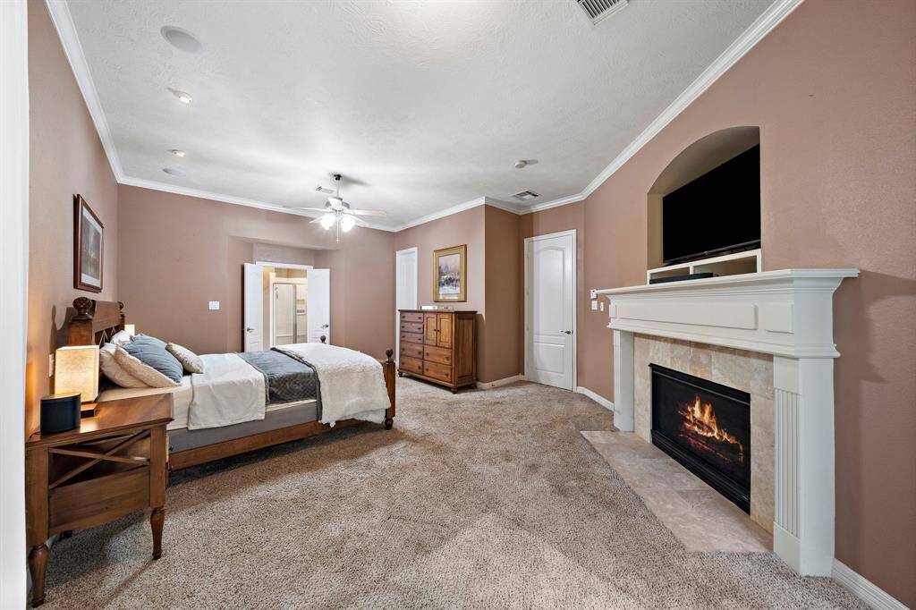 The primary suite impresses with its soaring ceilings, refined crown molding, and soft carpeted floors, complemented by a charming gas log fireplace.