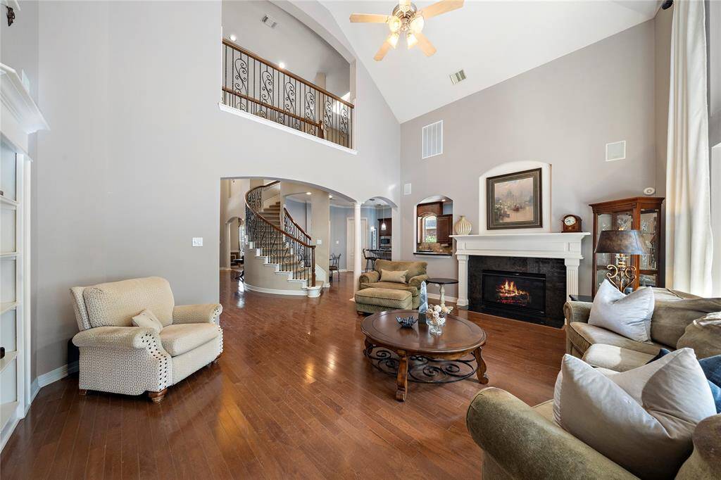 The living area is a harmonious blend of comfort and elegance, boasting soaring ceilings, expansive windows, and rich wood flooring. A gas log fireplace serves as the centerpiece, surrounded by large windows that fill the space with natural light, creating a cozy ambiance ideal for both relaxing evenings and lively gatherings.