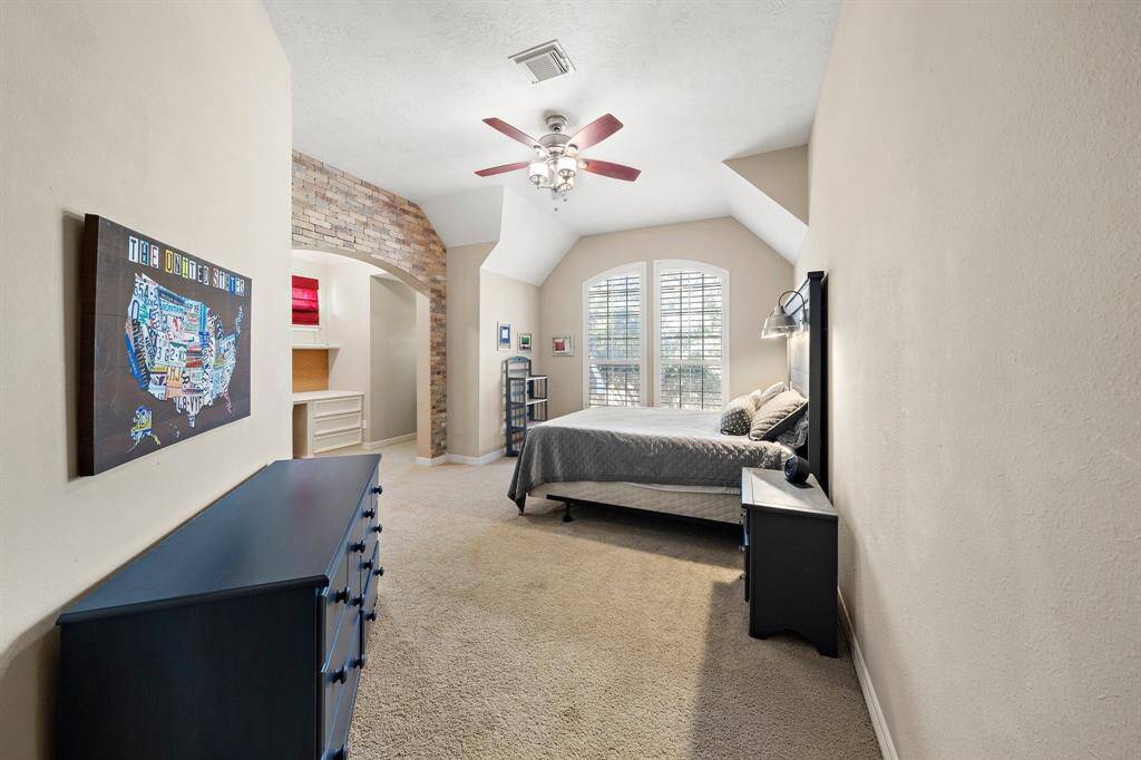 This secondary bedroom offers an inviting haven with ample floor space and a striking accent wall. Large windows flood the room with natural light, while a built-in desk and shelving nook enhance its functionality, making it perfect for both comfort and productivity.