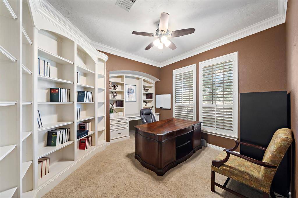 Bright and spacious, the executive home office features custom bookcases, carpet flooring, and plenty of space for a desk, additional seating, and cabinetry.
