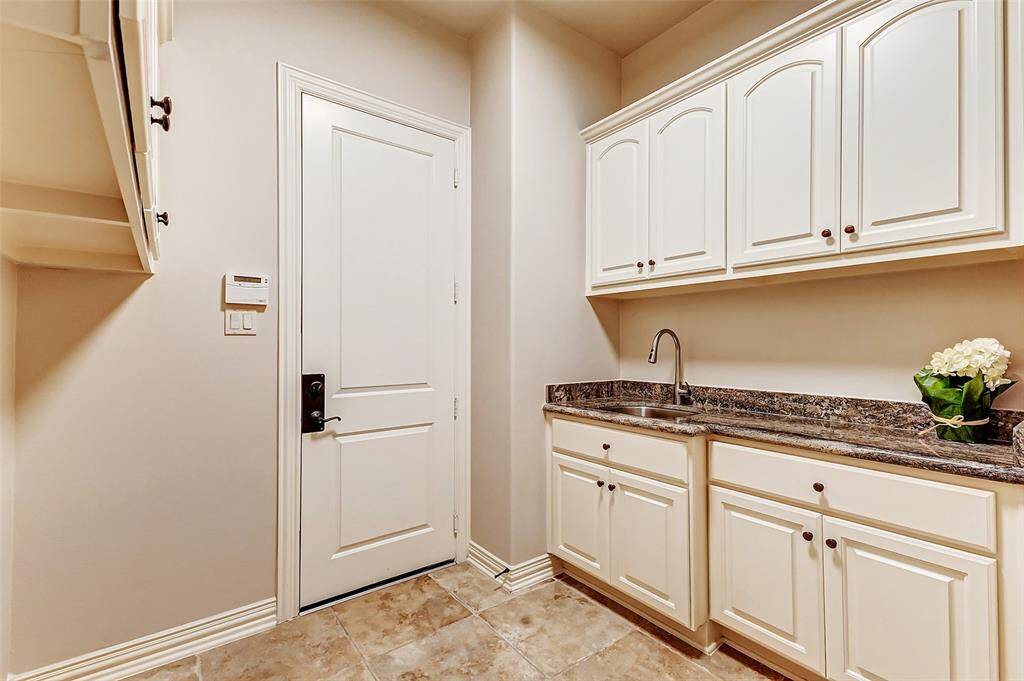 Well-appointed utility room featuring two walls of cabinetry for ample storage, granite countertops, and an upgraded sink faucet. Includes clothes hanging, gas and electric dryer connections, and electric and water for a second refrigerator. Conveniently provides direct garage access and an alarm keypad for security