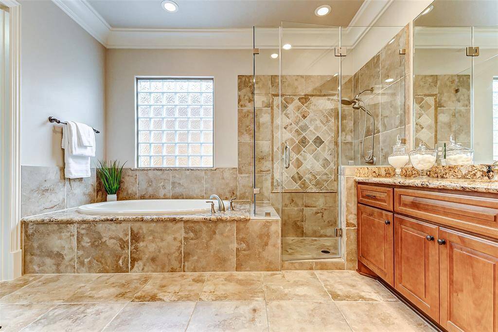 Indulge in luxury in this spa-like primary bathroom featuring an air jet soaking tub, an oversized frameless glass shower with custom tile work, and upgraded shower hardware. Additional ceiling lights brighten the space, creating a serene retreat. The textured glass block window allows natural light while maintaining privacy.