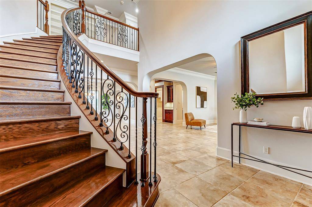 Grand curved staircase with elegant wrought iron balusters and rich wood handrails creates a stunning focal point in the entryway. Beautifully crafted wood treads contrast with the neutral-toned tile flooring, enhancing the home's sophisticated ambiance. Walk in closet under the stairs for additional storage.