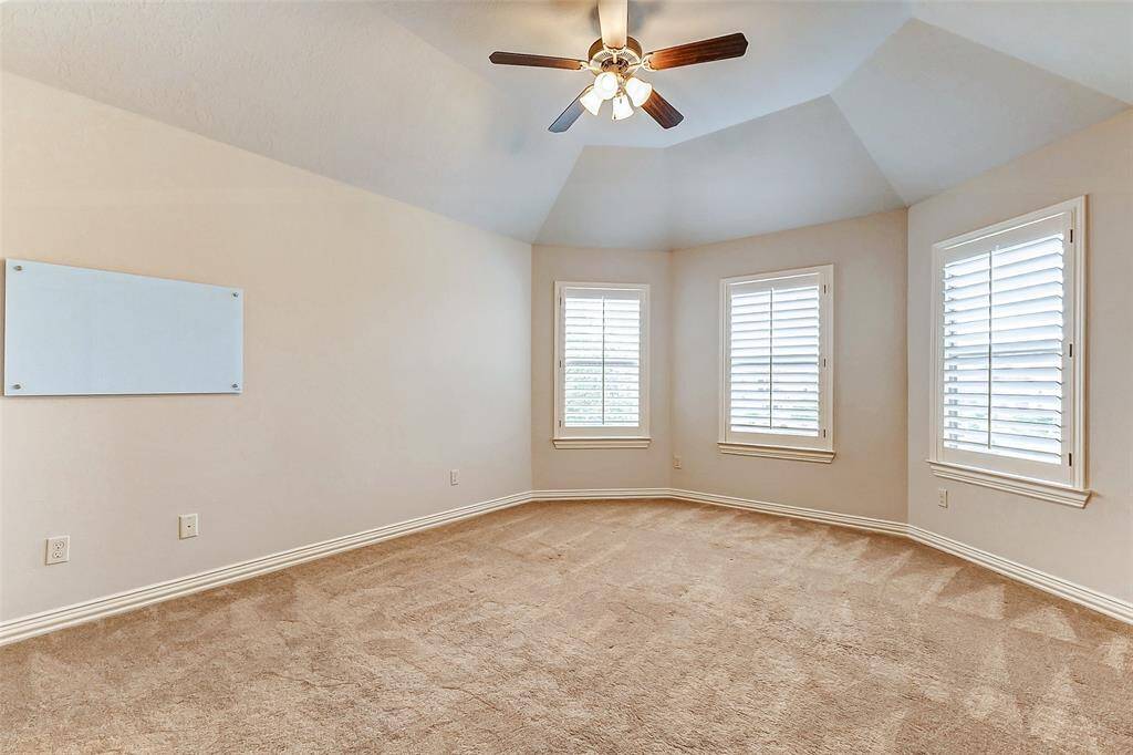 This inviting secondary bedroom offers a generous layout with a beautiful vaulted ceiling and ample natural light streaming through three large windows adorned with plantation shutters. The plush carpeting adds warmth and comfort, making it an ideal retreat. A ceiling fan enhances air circulation, ensuring year-round comfort.