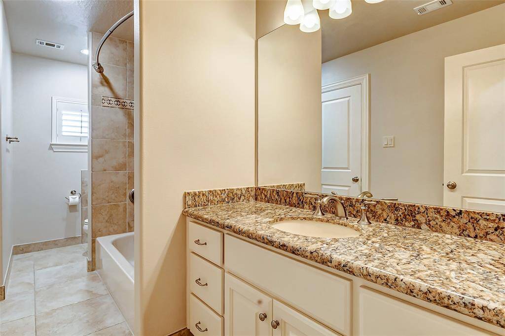 Connected to the bedroom is a well-appointed en-suite bathroom featuring a granite-topped vanity with ample storage, a bathtub with elegant tile surround, and brushed nickel fixtures. This bathroom also provides convenient hallway access. The thoughtful layout ensures both privacy and accessibility, catering to a variety of needs.