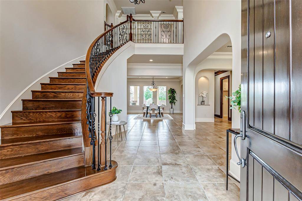 Step through grand double mahogany doors into a breathtaking two-story foyer featuring a sweeping spiral staircase with wrought iron balusters. A stunning chandelier casts an elegant glow over the space, highlighting the upgraded Italian porcelain tile flooring. Recent interior and exterior paint enhance the home's timeless charm, creating a welcoming first impression of refined luxury.
