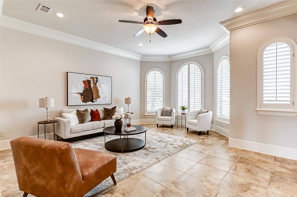 Elegant living area featuring plantation shutters, 12-inch crown molding, and 8-inch baseboards, adding a touch of sophistication. This spacious room offers versatility and can easily function as a formal dining room. The sellers have switched light fixtures and furnishings to accommodate different layouts, showcasing the room’s flexibility.