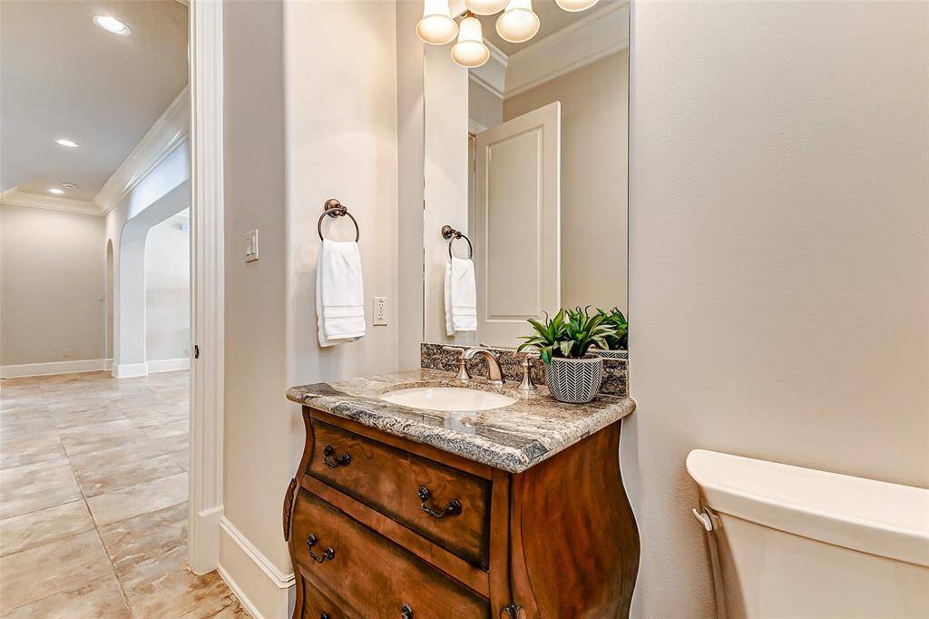 Charming half bath with an elegant furniture-style vanity is topped with a granite countertop. The updated fixtures, and warm neutral tones create a welcoming yet sophisticated feel. Ideally located for guests, this powder room offers both style and convenience.