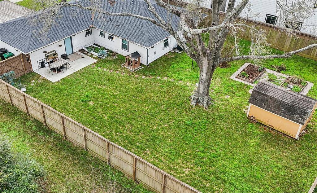 Spacious backyard featuring a patio slab, large tree for shade, a garden space, and a storage shed. The yard is fully enclosed by a wooden fence, offering privacy and ample green space for outdoor activities.