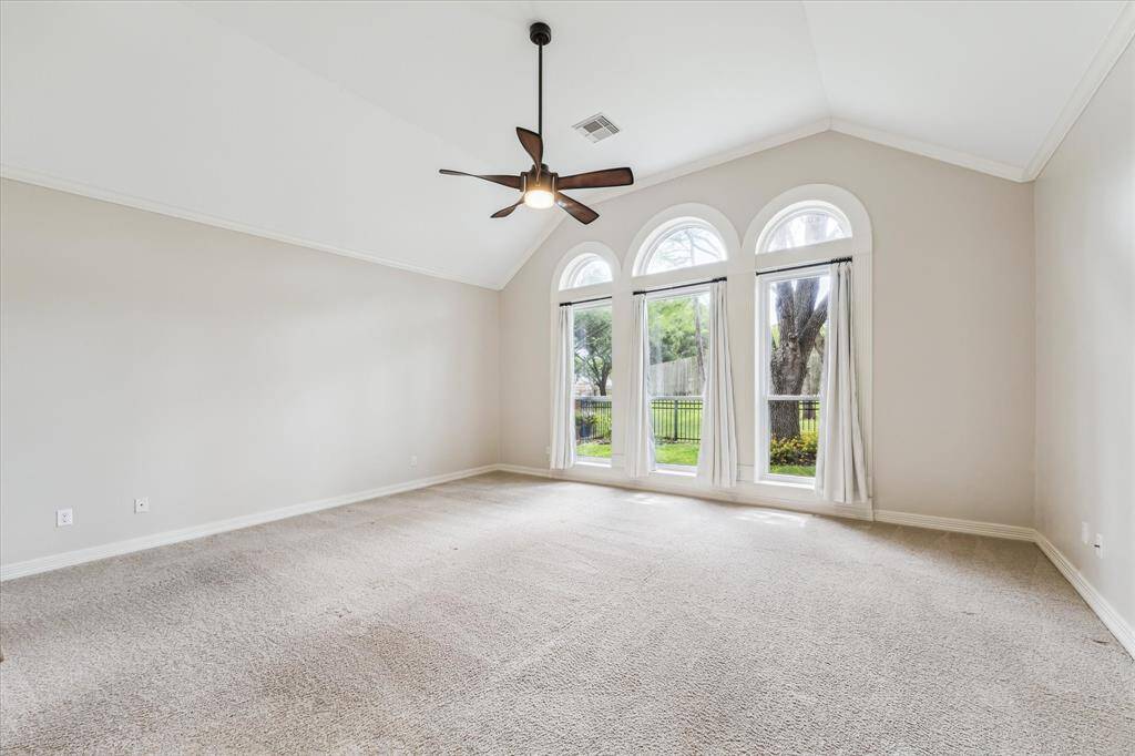 Triple windows with arched transom accent, carpet floor, high ceiling and crown molding are features of the lower level primary bedroom that is located at the rear of the home.