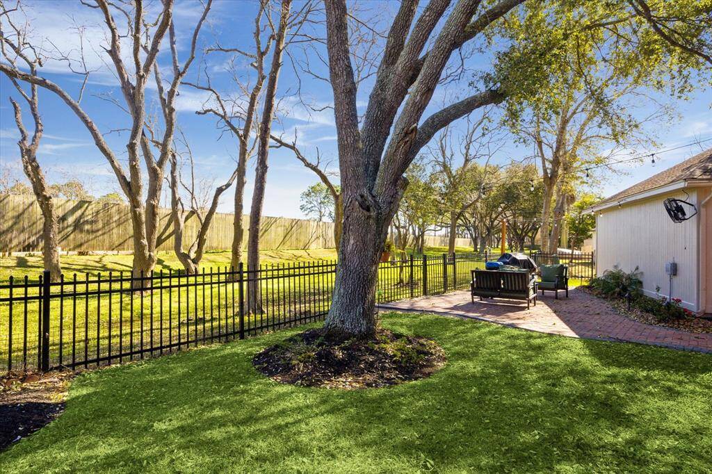 This view across the backyard shows another view of the additional patio area at the rear of the detached garage and a view of the back greenspace and wrought iron fence. The accessible greenspace has a walking trail that leads to the community park & pool at the end of the block and continues to Ferguson Elementary School.