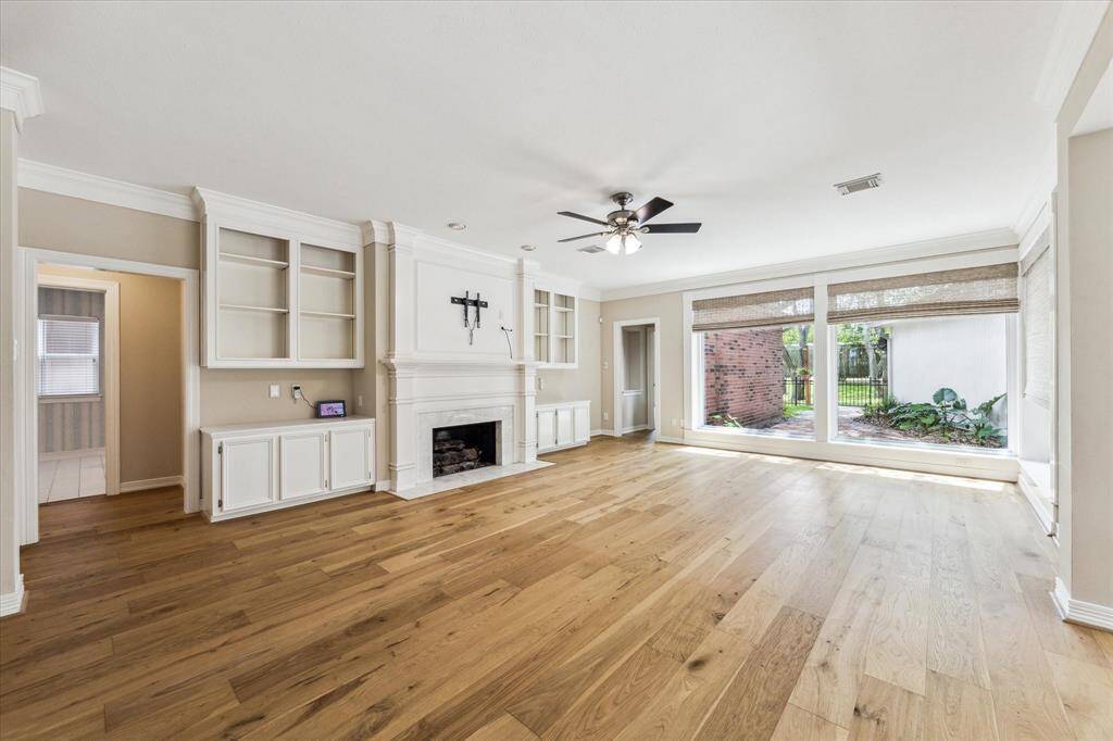 The family room is located at the rear of the lower level and features oversize double windows overlooking the back patio and lawn area. This photo also shows the updated engineered wood flooring. The family room has a wood burning fireplace with gas logs, custom tile surround and wooden mantle. Another feature is the built-in upper level open shelving and lower level cabinet storage at each side of the fireplace.