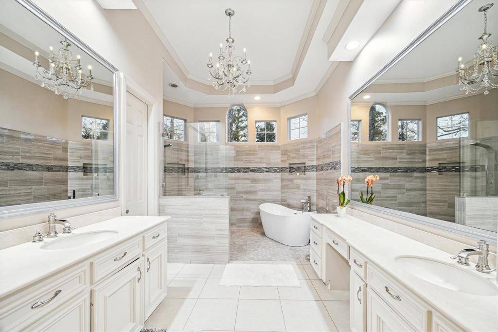 The primary en suite bathroom is a breathtaking escape with long white counters and cabinets and expansive mirrors reflecting the designer light fixtures.