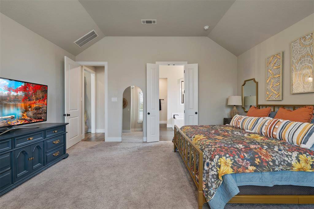 There is another spacious, well-lit bedroom with neutral walls, plush carpeting, and a vaulted ceiling. The room opens to a bathroom, enhancing its functionality and appeal.