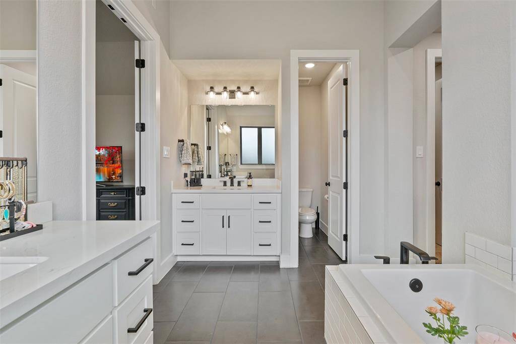 This bathroom with a dual-sink vanity, sleek cabinetry, and a built-in bathtub. The space features neutral tones and ample natural light.