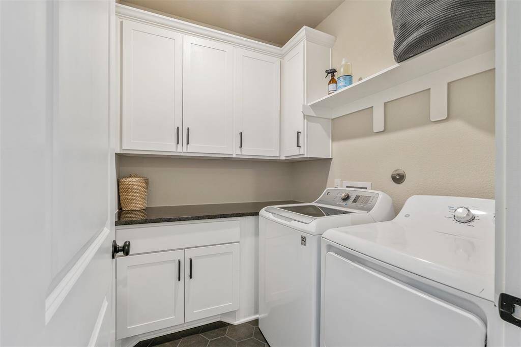 Great laundry room featuring white cabinetry, a black countertop. The space is organized with additional shelving for storage and has a clean, neutral color palette.